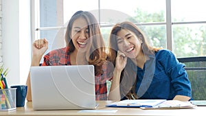 Two young asian women working with laptop computer at home office with happy emotion moment, working at home, small business,