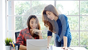 Two young asian women working with laptop computer at home office with happy emotion moment, working at home, small business,