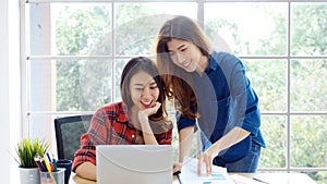 Two young asian women working with laptop computer at home office with happy emotion moment, working at home, small business,