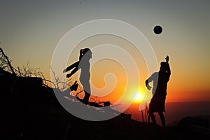 Two young athletes man and woman aged 25-30 playing volleyball on top of the mountain at sunset. Sports moment. Active life.