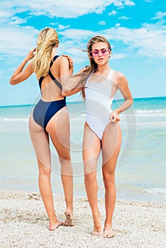 Two young attractive girls with long hair in a swimsuits relax on beach in the sea