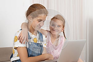 Two young attractive girls teenager with red hair  lies on a sofa at home using laptop