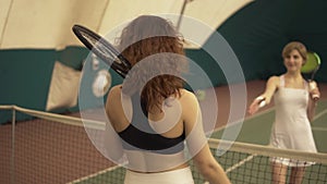 Two young attractive tennis players shake hands near the net at the tennis court. Sports and recreation.