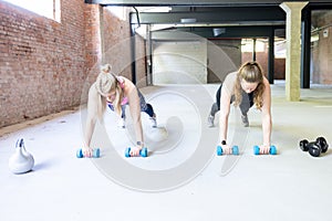 Two young attractive women doing push ups inside with barbells. Fitness woman working out in a cross fit gym. Fitness