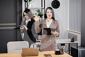 Two young attractive women are working in the office. A woman is talking on the phone, and her colleague is making notes in a