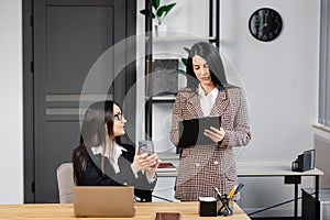 Two young attractive women are working in the office. A woman is talking on the phone, and her colleague is making notes in a