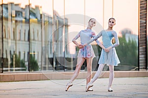 Two young ballerinas in pointe shoes are dancing against background of the reflection of the city sunset in mirrored wall of