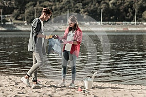 Two young beaming students standing near the river while cleaning the sand