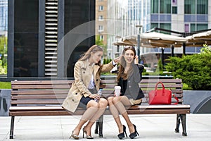 Two young beautiful business women sitting on a bench