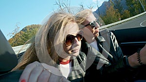 Two young beautiful girls in black glasses and leather jackets ride in a red cabriolet near the high mountains. Life is
