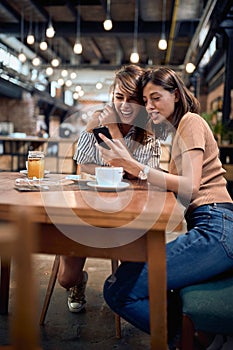 Two young beautiful girls in cafe having a great time. Woman showing something on her phone