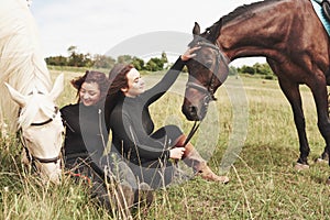 Two young beautiful girls in gear for riding near their horses. They love animals