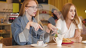 Two young beautiful girls girls drink tea in a summer cafÃ©. Girlfriends have breakfast in a cafÃ©, drink coffee