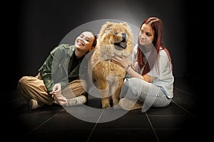 Two young, beautiful girls are having fun with a chow chow dog