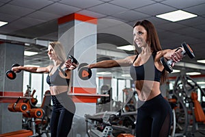 Two young, beautiful girls perform lifting dumbbells through the sides. gym.