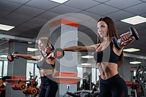 Two young, beautiful girls perform lifting dumbbells through the sides. gym.