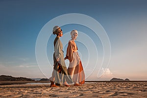 Two young beautiful girls in turban walking on the beach at sunset