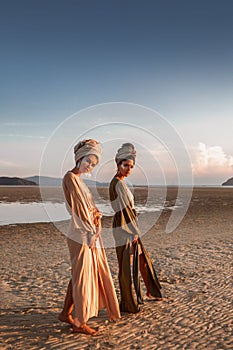 Two young beautiful girls in turban walking on the beach at sunset
