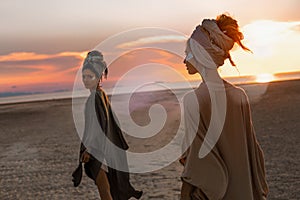 Two young beautiful girls in turban walking on the beach at sunset