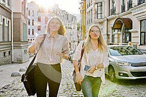 Two young beautiful happy women university students walking along city street