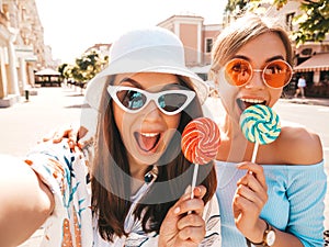 Two young beautiful smiling hipster girls in trendy summer clothes