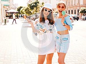 Two young beautiful smiling hipster girls in trendy summer clothes