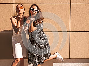 Two young beautiful smiling hipster girls in trendy summer clothes