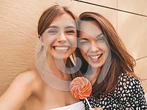 Two young beautiful smiling hipster girls in trendy summer clothes