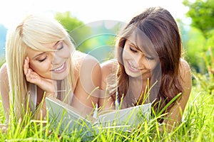 Two young beautiful smiling women reading book