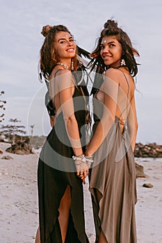 Two young beautiful stylish boho girls on the beach at sunset