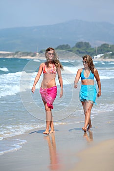 Two young beautiful tanned women walking along sandy beach