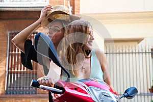 Two young, beautiful touring women are riding a red motorbike. The women are happy and having fun looking at the camera and