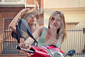 Two young, beautiful touring women are riding a red motorbike. The women are happy and having fun looking at the camera and