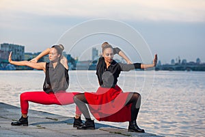 Two young beautiful twin sisters are dancing waacking dance in the city background near river.