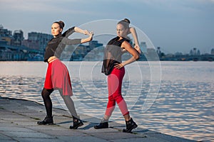 Two young beautiful twin sisters are dancing waacking dance in the city background near river.