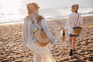 Two young beautiful women female friends going to have summer picnic on a beach at sunset