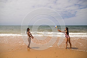 Two young and beautiful women playing boley on the shore of the beach. The women are enjoying the game and their day at the beach