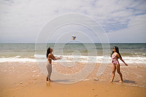 Two young and beautiful women playing boley on the shore of the beach. The women are enjoying the game and their day at the beach