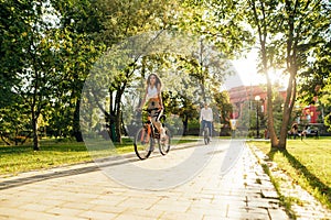 Two young bicyclist are racing in the park on a sunny day, a man is following a woman. Friends in casual sport outfits on fancy
