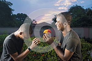 two young black gay couple laughing, one giving his partner flowers as a surprise