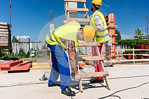 Two young blue-collar workers leaning a ladder