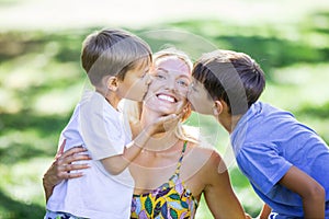 Two young boys kissing their mother outdoors