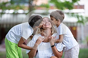 Two young boys kissing their mother in summer park