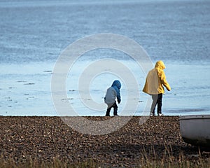 Two young boys in rain coats playing at the coast