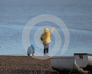 Two young boys in rain coats playing at the coast