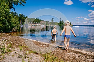 Two young boys in swimming trunks run along the lake shore on a summer day