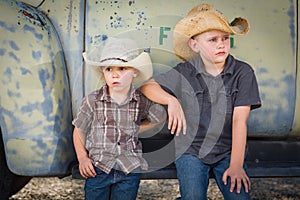 Two Young Boys Wearing Cowboy Hats Leaning Against an Antique Truck in a Rustic Country Setting