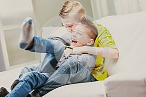 Two young brothers laughing as they romp on the couch