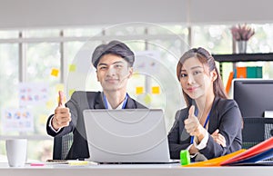 Two young business colleagues showing thumbs up and looking at camera, Smiling business people in modern office