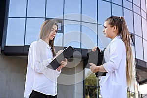 Two young business ladies posing outside office building. Women and business